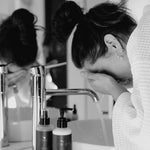 A Woman washing her face in a bathroom sink with Reign Green Tea and Lemongrass Cream Cleanser