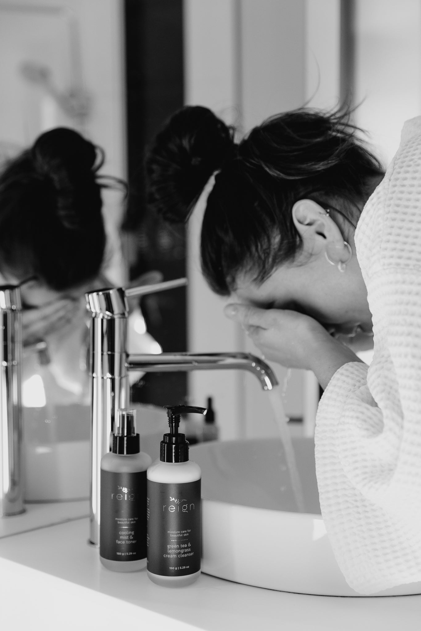 A Woman washing her face in a bathroom sink with Reign Green Tea and Lemongrass Cream Cleanser