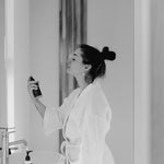 A woman spraying Reign Cooling Face Mist and Toner onto her face in a bathroom