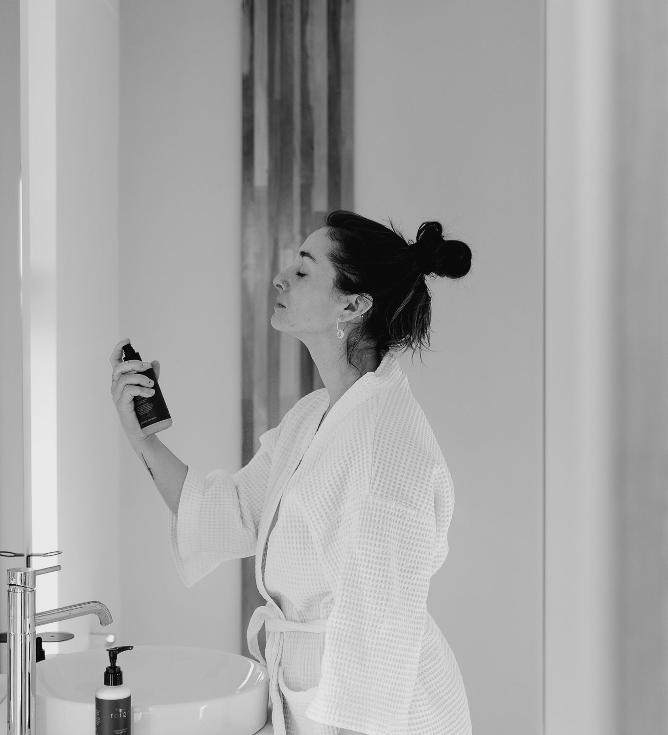 A woman spraying Reign Cooling Face Mist and Toner onto her face in a bathroom