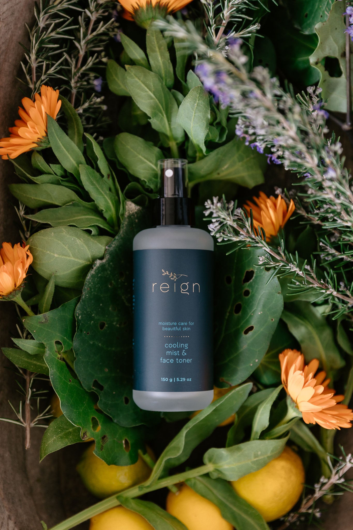 Blue bottle of 'reign' cooling face toner surrounded by green leaves and orange calendula flowers