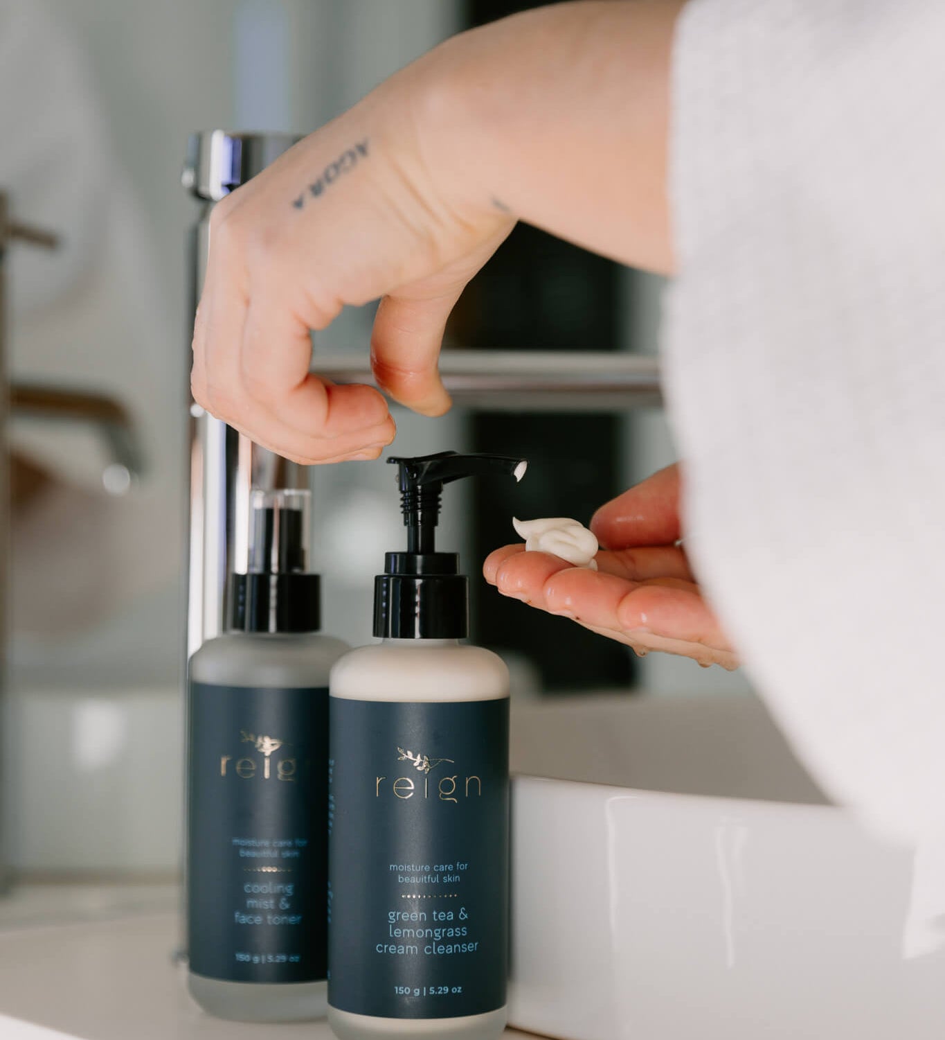 Person using a pump bottle of Reign Green tea and lemongrass cleanser product in a bathroom setting.