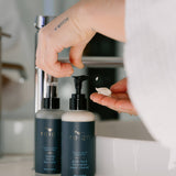 Person using a pump bottle of Reign Green tea and lemongrass cleanser product in a bathroom setting.