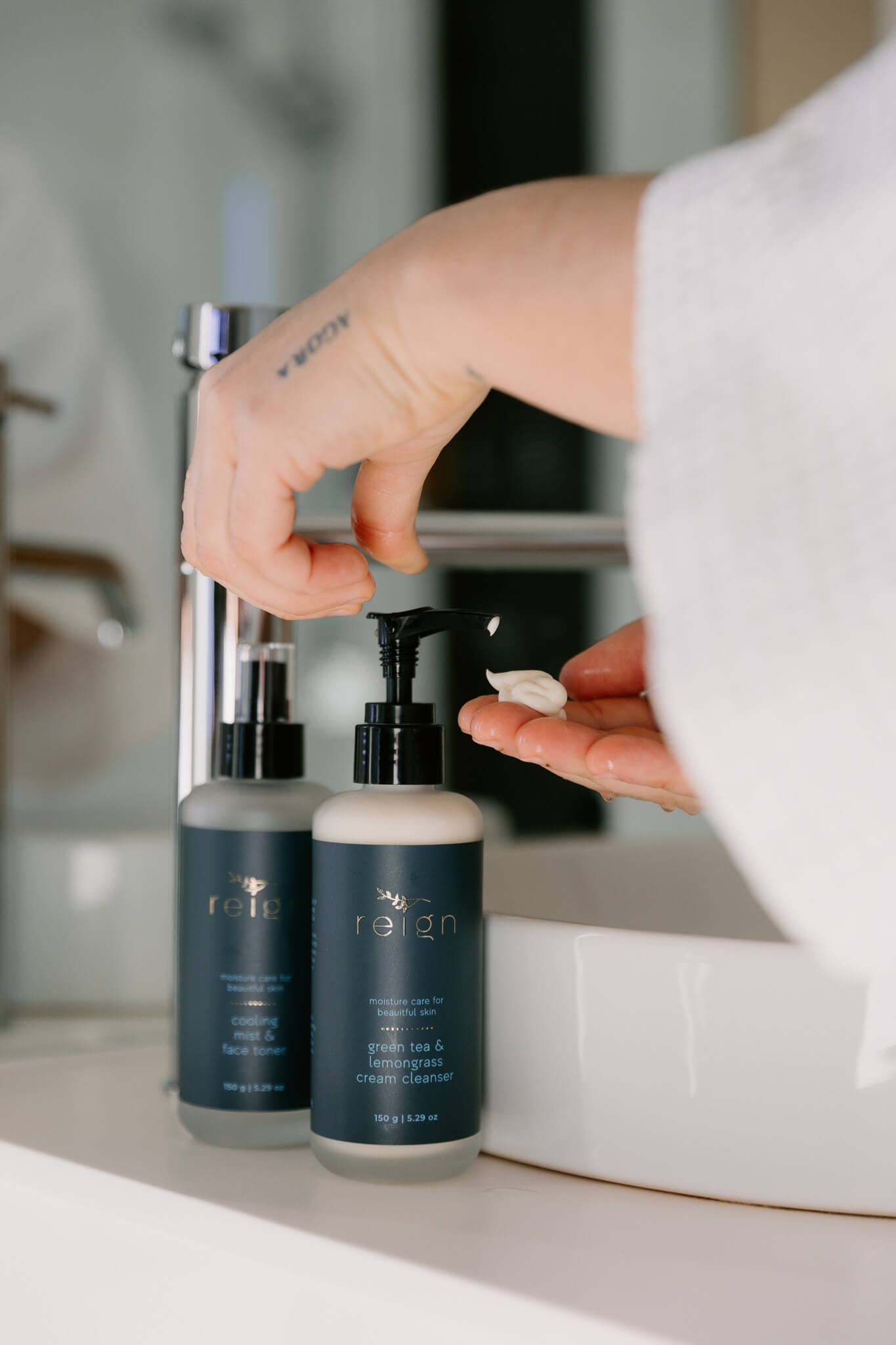 Person using a pump bottle of Reign Green tea and lemongrass cleanser product in a bathroom setting.