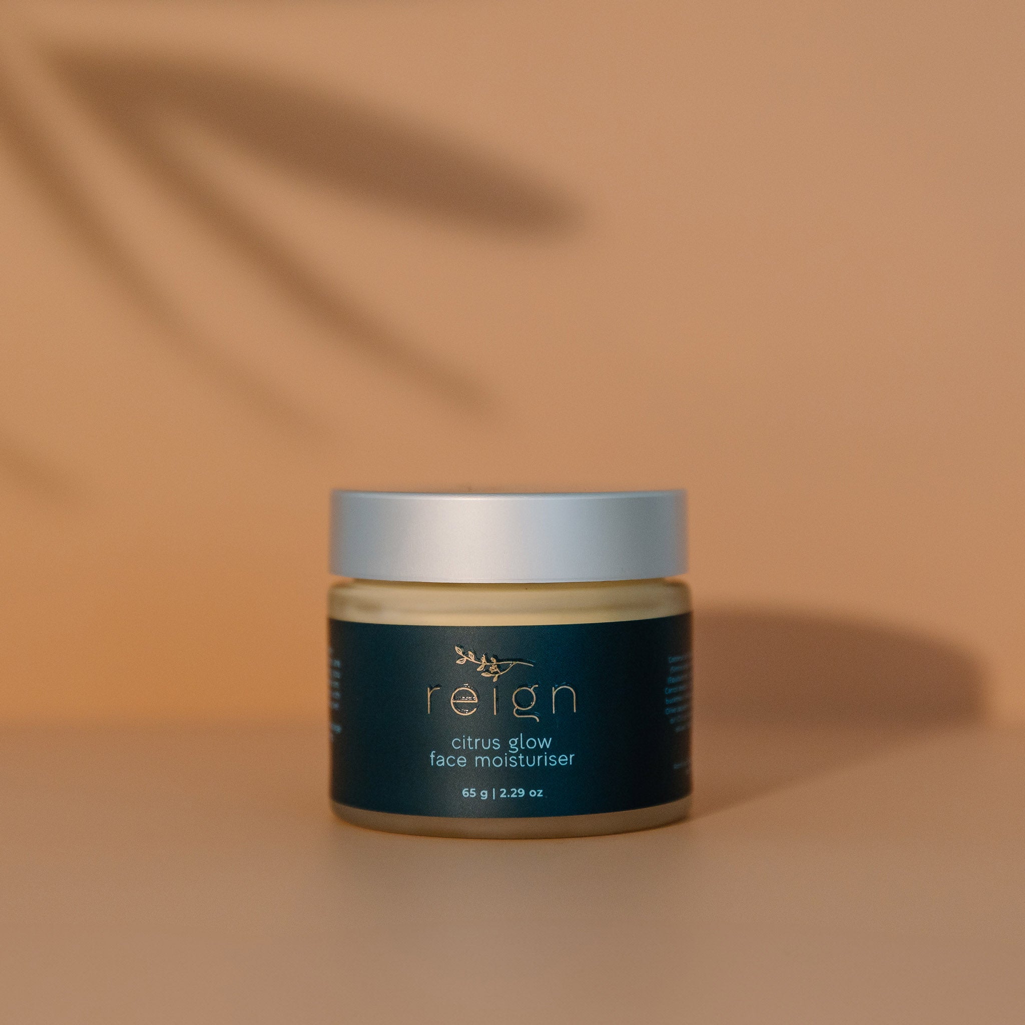 Jar of Reign Citrus Glow face moisturiser with 'reign' branding on a warm background