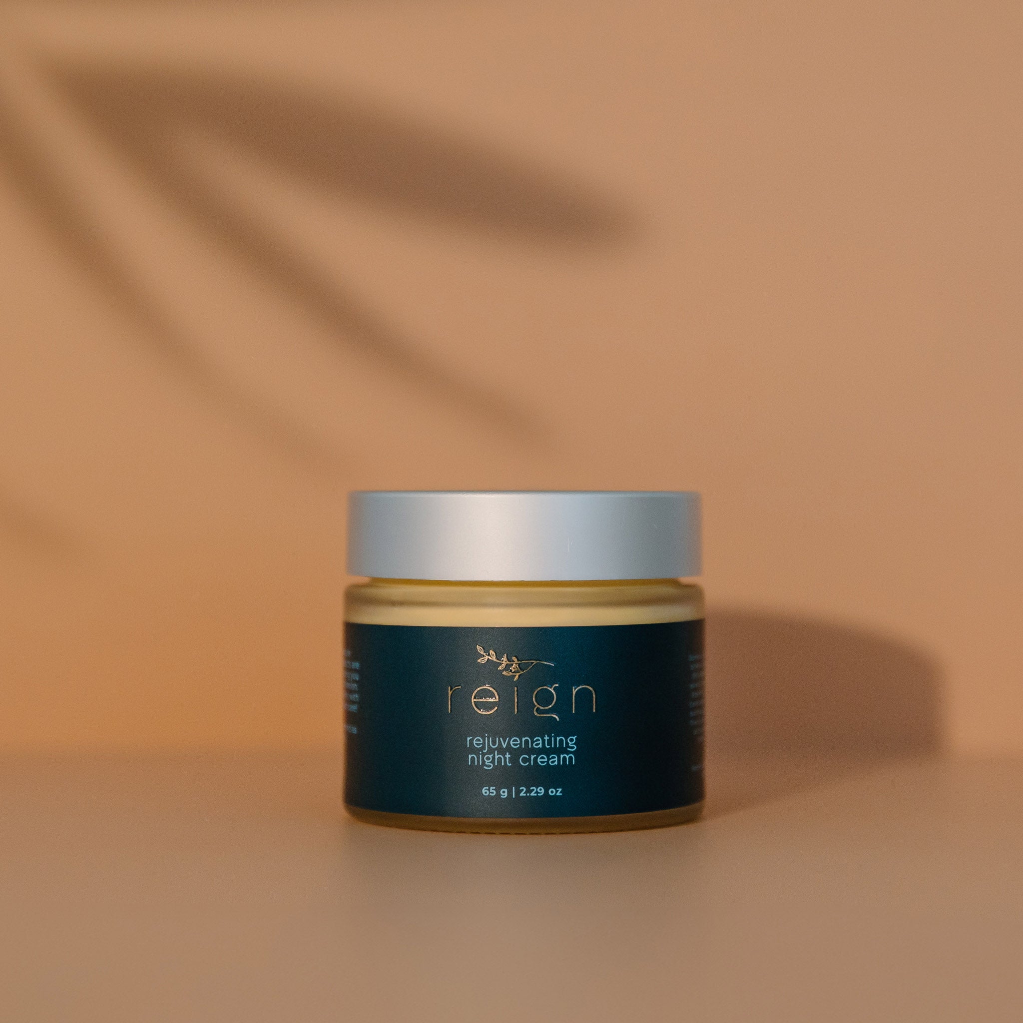Jar of Reign rejuvenating night cream with a dark label on a warm background